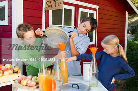 Teenage boy and siblings pouring fresh orange juice to sell at roadside