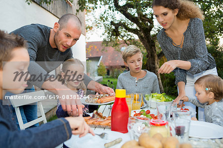 Father and teenage girl helping children at garden barbecue table