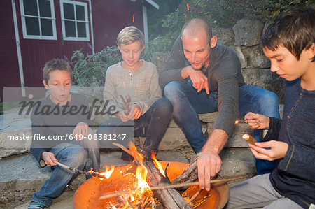 Father and three sons sitting by garden campfire at dusk