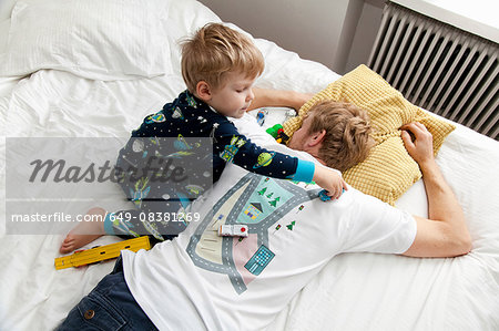 Young boy playing with toy car on back of fathers tshirt in bed
