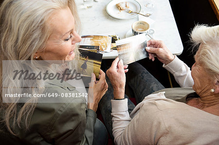 Mother and daughter sitting together in cafe, looking at photographs, rear view