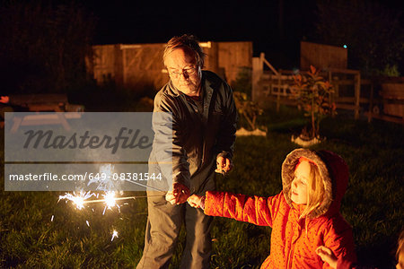 Senior man in garden handing sparkler to girl