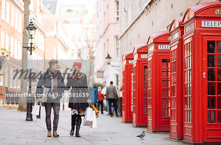 Young shopping couple strolling past red phone boxes, London, UK