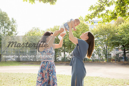 Young woman and mother holding up baby girl in park