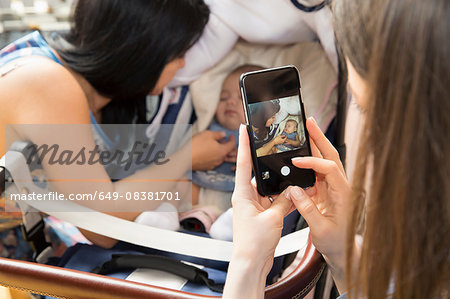 Young woman photographing mother and baby daughter on smartphone