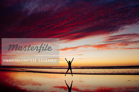 Rear view of nude mid adult womans silhouette jumping, in mid air, legs apart arms raised Rear view of nude mid adult womans silhouette jumping, in mid air, legs apart arms raised