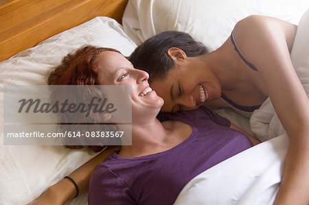High angle view of lesbian couple lying in bed hugging, smiling