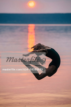 Side view of girl by ocean at sunset, leaping in mid air bending backwards