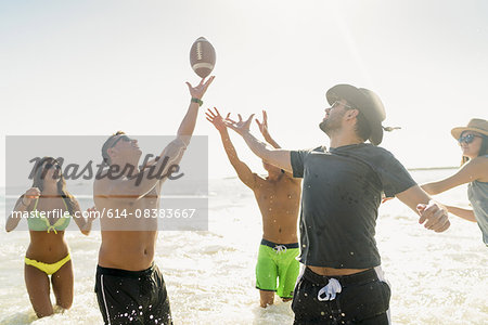 Male and female adult friends playing American football in sea at Newport Beach, California, USA