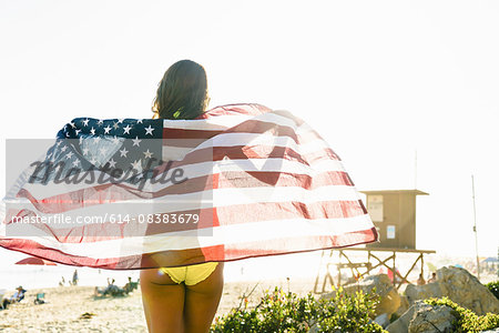 Rear view of young woman wrapped in American flag on Newport Beach, California, USA