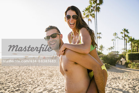 Portrait of young man giving girlfriend a piggyback on Newport Beach, California, USA