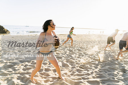 Male and female adult friends playing American football on Newport Beach, California, USA