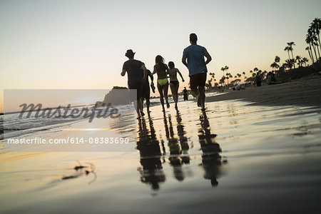 Rear view of adult friends running on beach at sunset, Newport Beach, California, USA