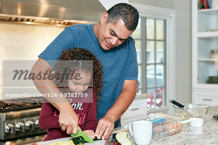 Father helping daughter chop vegetables in kitchen