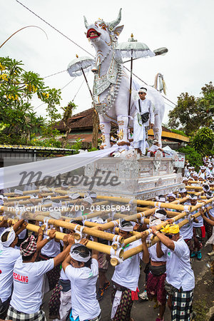 People carrying a raised, white bull character in a parade at a cremation ceremony for a high priest in Ubud, Bali, Indonesia