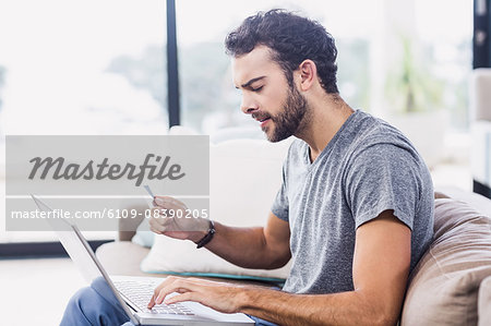 Handsome man holding credit card ad using laptop