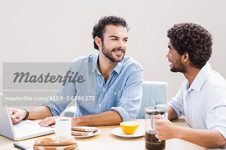 Happy gay couple having breakfast and using laptop