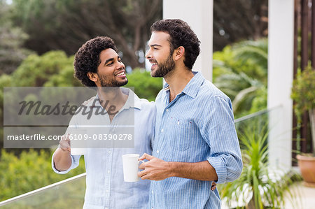 Smiling gay couple holding cups and talking
