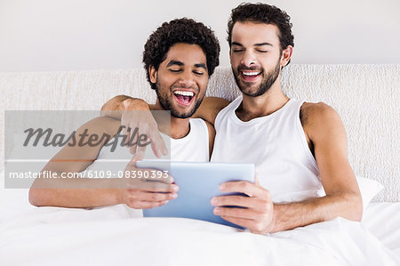 Happy gay couple using tablet on bed