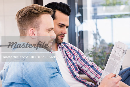 Gay couple relaxing on the couch reading newspaper