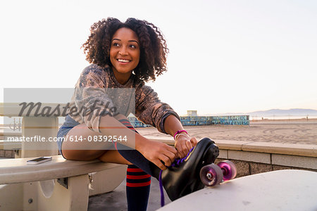 Mid adult woman sitting outdoors, tying rollerskates