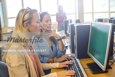 Two women searching computer data for books in library