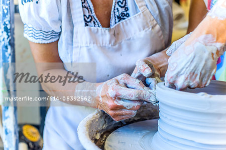 Close up of hands of female potter and mature student making pot on potters wheel