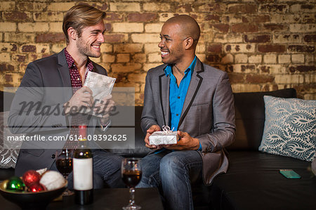 Male couple sitting on sofa, exchanging Christmas gifts