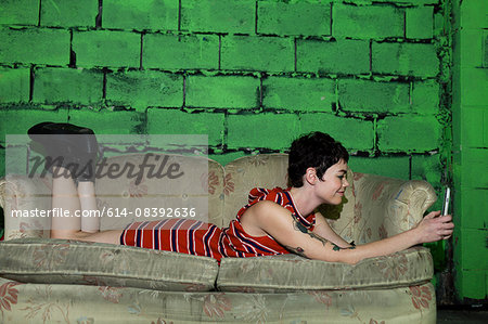 Mid adult woman relaxing on worn sofa, using smartphone