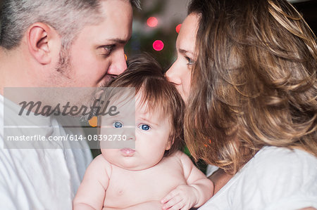 Mother and father face to face holding baby girl, kissing on head