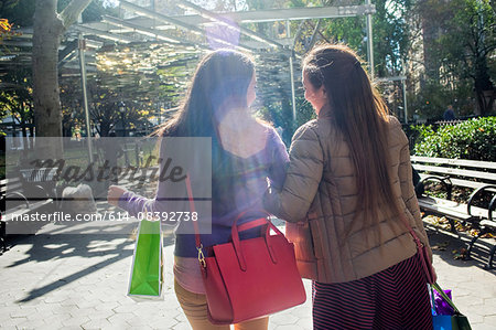 Rear view of young female adult twins strolling in park with shopping bags