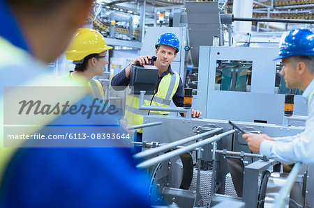 Workers talking at machinery in factory Workers talking at machinery in factory
