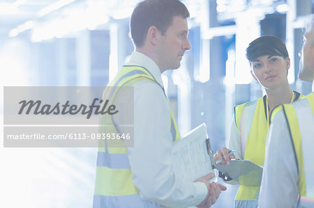 Workers in reflective with clipboards talking in factory