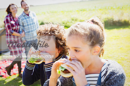 Brother and sister eating hamburgers at sunny campsite
