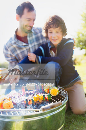 Father and son barbecuing hamburgers and vegetable skewers