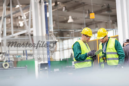 Workers in protective workwear talking with clipboard working in factory