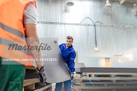 Workers carrying sheet metal in factory