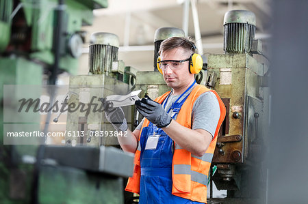 Worker in protective workwear examining part in factory