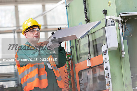 Worker in protective workwear examining steel part in factory