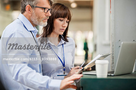 Business people with clipboard working at laptop in factory