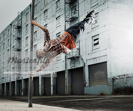 A young man breakdancing, leaping in the air, and stretching out.
