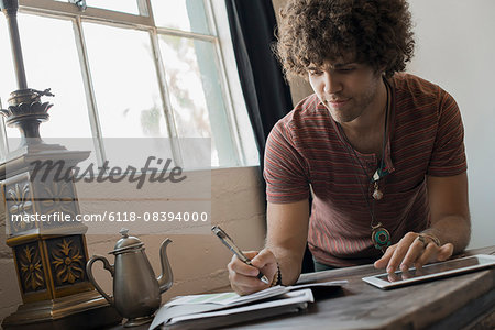 Loft living. A man seated by  window, using a pen and paper and a digital tablet.