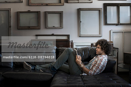 Loft decor. A wall hung with blank canvases. A man on a sofa using a digital tablet.