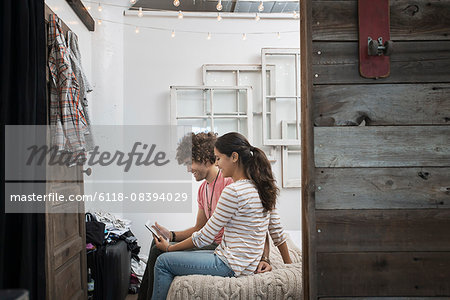 Loft living. Two people a man and woman sitting on a bed looking at a digital tablet.