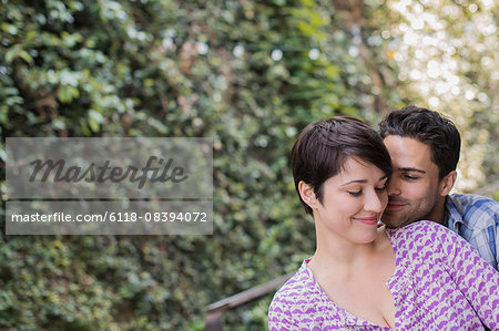 A couple in a city park beside a green wall of foliage embracing.