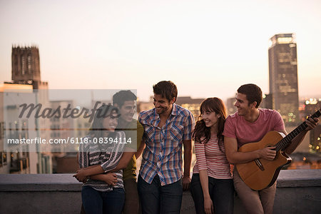 A small group of friends gathered on a rooftop terrace overlooking a city at twilight.