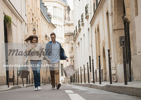 A couple walking along a narrow street in a historic city centre, with shopping bags.