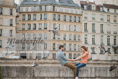 A couple, man and woman sitting on the parapet of a bridge over the River Seine.