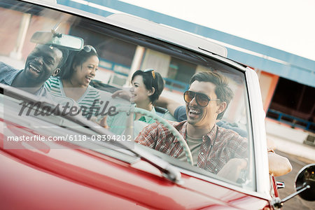 A group of friends in a red convertible car on a road trip.