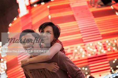 A man giving a woman a piggyback, under a bright neon Casino sign.